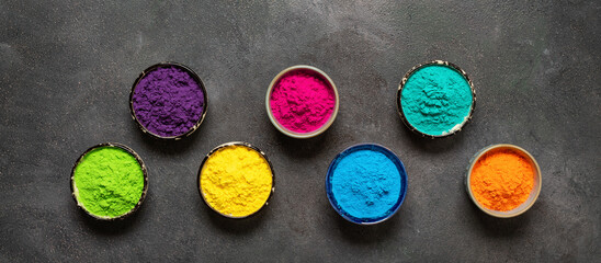 Colored organic holi powders in bowls on a dark background. View from above. Banner.