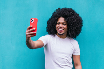 Exuberant Afro-Latino man enjoying the moment, capturing a selfie with his red phone against a...