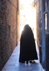 Tapeten Enge Gasse anonymous hooded stroller with black cloak dress walking through the narrow alleys