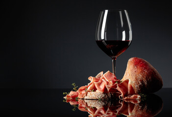 Prosciutto with ciabatta, red wine and thyme on a black background.