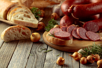 On a old wooden table sausage with bread, rosemary, onion and pepper.