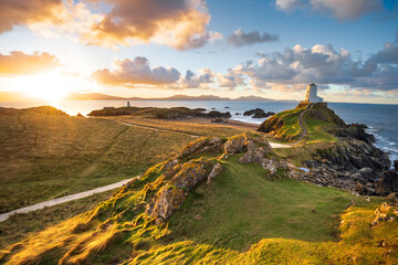 Golden sunrise at Twr Mawr Lighthouse on Ynys Llanddwyn Island on The Coast of Anglesey, North Wales with Snowdonia mountains in background. - 738681814