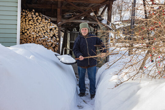 A pensioner paves a path through snowdrifts to a wood shed. Snowy winter