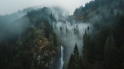 Aeriel view of waterfall between trees of high hills in a foggy day. Water flows down to rocky mountain.