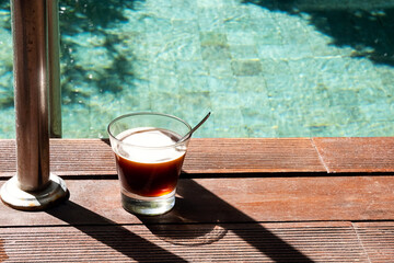 Morning coffee at poolside. Coffee glass standing near swimming pool.