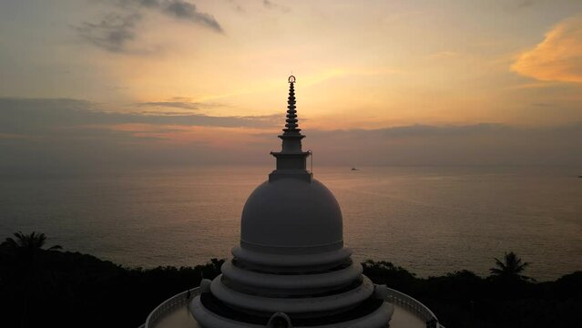 White pagoda buddhist temple top among the jungle at sunset. Japanese Peace Pagoda spire in Sri Lanka aerial view.