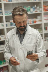 Male pharmacist in white coat holding nose spray and blister with pills while working at a pharmacy