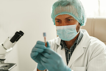 Scientist in mask is holding test tube at laboratory. Medicine and research in chemistry