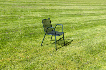 Ein Metallstuhl in der Mitte des Rasenfeldes. Das Konzept von Einsamkeit und Leere.