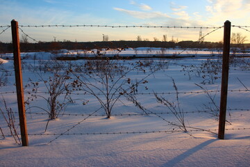 View of a closed industrial area behind a barbed wire fence in winter at sunset