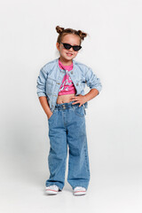 Kid in pink t-shirt and jeans and sunglasses in studio. Full length portrait little girl with hairstyle buns