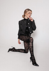 beautiful woman with blond hair in elegant patterned tights and jacket posing in studio - 738696805