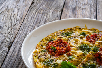 Tagliatelle omelet - scrambled eggs with mozzarella cheese, tagliatelle, basil and tomato pesto on wooden table
