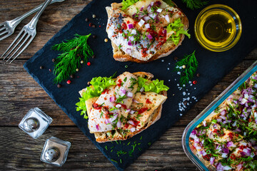 Tasty sandwiches - toasted bread with pickled herrings and red onion on wooden table
