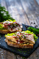 Tasty sandwiches - toasted bread with pickled herrings and red onion on wooden table
