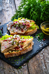 Tasty sandwiches - toasted bread with pickled herrings and red onion on wooden table
