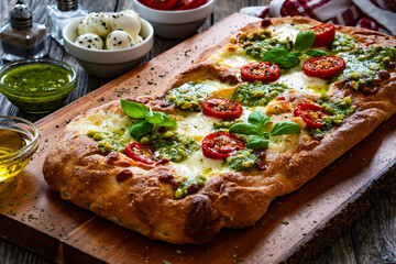 Pinsa Romana with mozzarella cheese and basil pesto on wooden table
