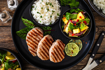 Grilled pork loin steaks with boiled white rice and mango salad on wooden table

