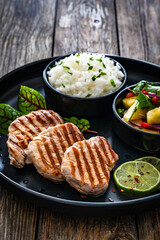Grilled pork loin steaks with boiled white rice and mango salad on wooden table
