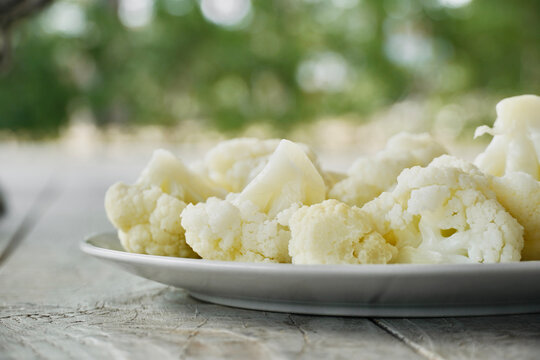 Organic cauliflower on white wooden table top with nature in the background.
