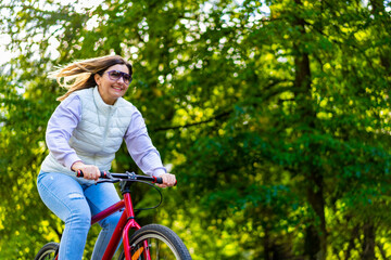Naklejka premium Mid-adult woman riding bicycle in city park 