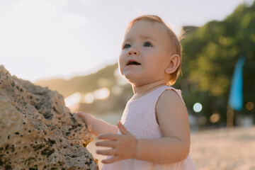 Portrait of cute baby girl in pink dress on beach with sunshine.