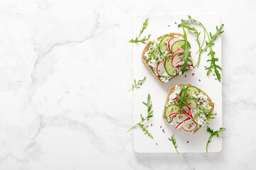 Sandwiches with rye bread toasts, cottage cheese, radish, cucumber, fresh greens and arugula for a healthy breakfast, top view - obrazy, fototapety, plakaty