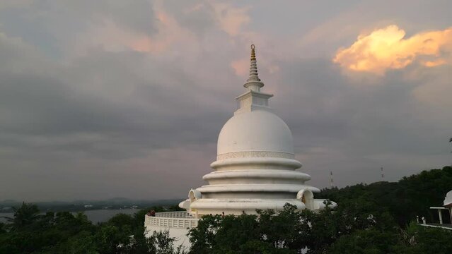 White pagoda buddhist temple among the jungle against the sunset clouds. Japanese Peace Pagoda in Sri Lanka aerial view.