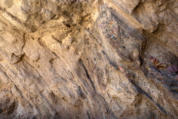 Textured background of rough uneven surface of stone with variety of colors and cracks.