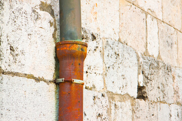 Old cast iron and copper downpipe against a stone wall - (Italy)