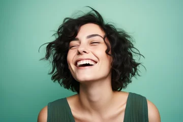 Poster Portrait of a happy young woman laughing with closed eyes over green background © Loli