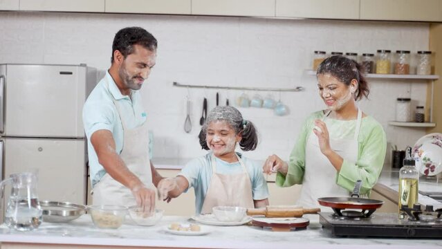 Playful Indian family with daughter plying flour while cooking at kitchen - concept of having fun, weekend holidays and relationship bonding
