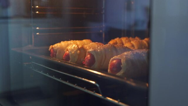 Baking sausage in dough on baking sheet in the oven, process of preparing sausages in dough at home