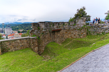 Castle hill of Ljubljana with stone walls and green grass with visitors on a cloudy summer day....