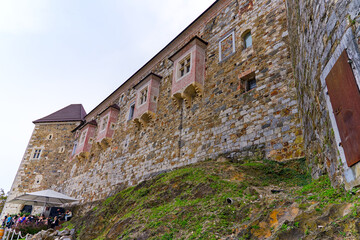 Looking up stone wall and tower with loophole of Castle of Ljubljana on a cloudy summer day. Photo taken August 9th, 2023, Ljubljana, Slovenia.