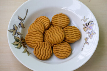 A white plate with some biscuits on a wooden background. Fresh healthy wheat cookies in round shape that are good for breakfast or evening snacks. 