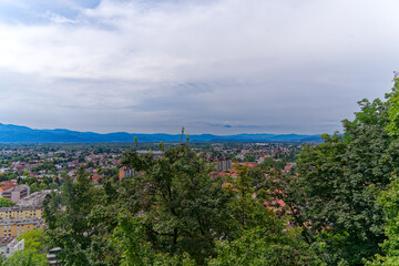 Fototapeta na wymiar Aerial view of City of Ljubljana seen from Sance castle hill with mountain panorama in the background on a cloudy summer day. Photo taken August 9th, 2023, Ljubljana, Slovenia.