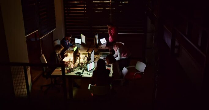 Dedicated businesspeople engage in collaborative work in a dimly lit office setting, illustrating their commitment during late hours, emphasizing their collective effort towards shared goals.