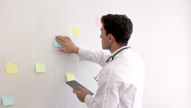 Caucasian young physician medical specialist work on schedule or analyse possible causes on whiteboard using paper note, child health care, experienced doctor examine African American female child