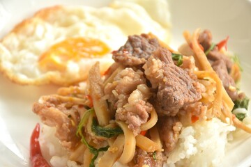 spicy stir fried bamboo shoot and slice beef meat with basil leaf topping egg on rice in plate  