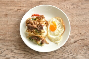 spicy stir fried bamboo shoot and slice beef meat with basil leaf topping egg on rice in plate  