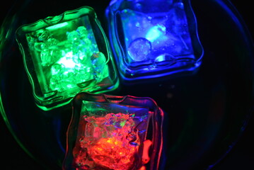 Beautiful, stylish photo of parties, celebrations, one glass champagne glass with glowing plastic ice cubes in drinks that glow with green, red and blue light.