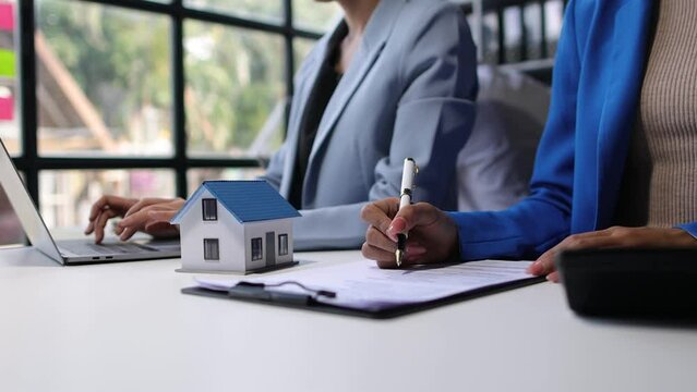 Businesswoman is negotiating the sale of house with real estate agent. Real estate agent is offering a house for sale, businessman signs agreement document.