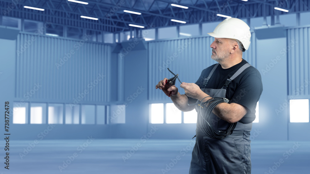 Poster electrician man inside hangar. installation of wiring in empty industrial building. builder man is p