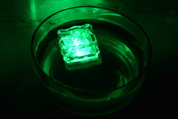 Beautiful, stylish photo of parties, celebrations, one glass champagne glass with glowing plastic ice cubes in drinks that glow green light.