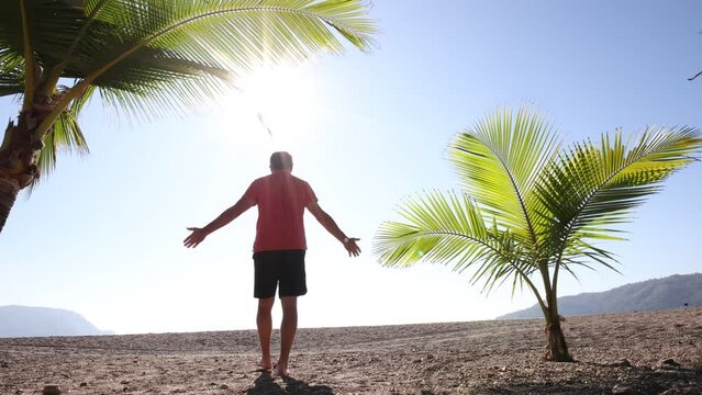 A middle-aged individual is relishing the tropical sun, ocean waves, and palm trees on a beach in the Pacific coast of Costa Rica.