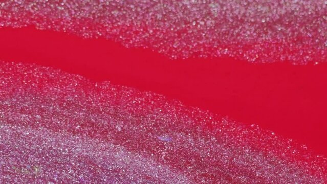Sparkling fluid. Glitter paint texture. Pink red color shiny metallic ink water spill mix wave motion on blur abstract free space background.
