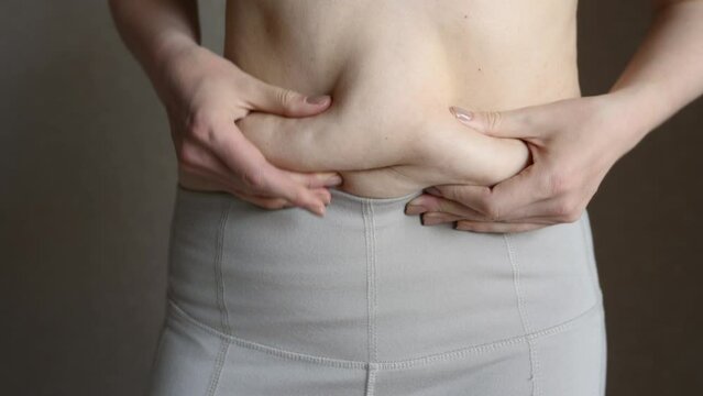 Overweight women pull white pants over their fat belly, touch their fat folds on their belly, close-up. Concept of overweight, obesity, diet, excess weight problems.