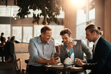 Businessmen using a smart phone while having a coffee at an indoor cafe in the city