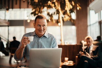 Mature businessman using a laptop at an indoor cafe while having a cup of coffee